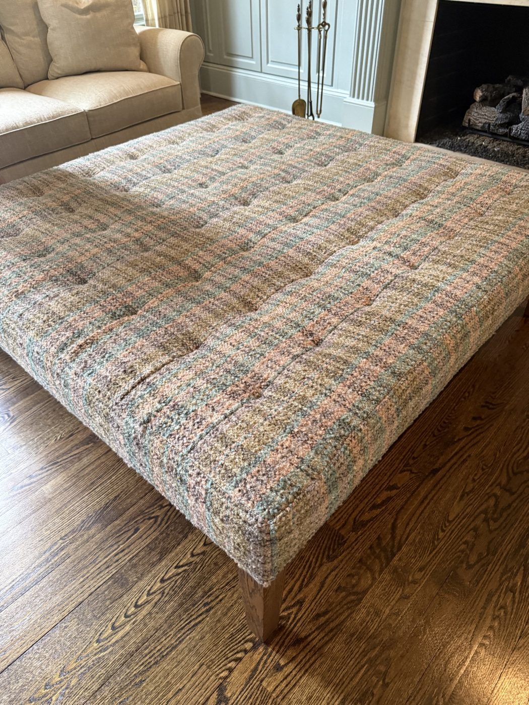 Tufted plaid ottoman by fireplace
